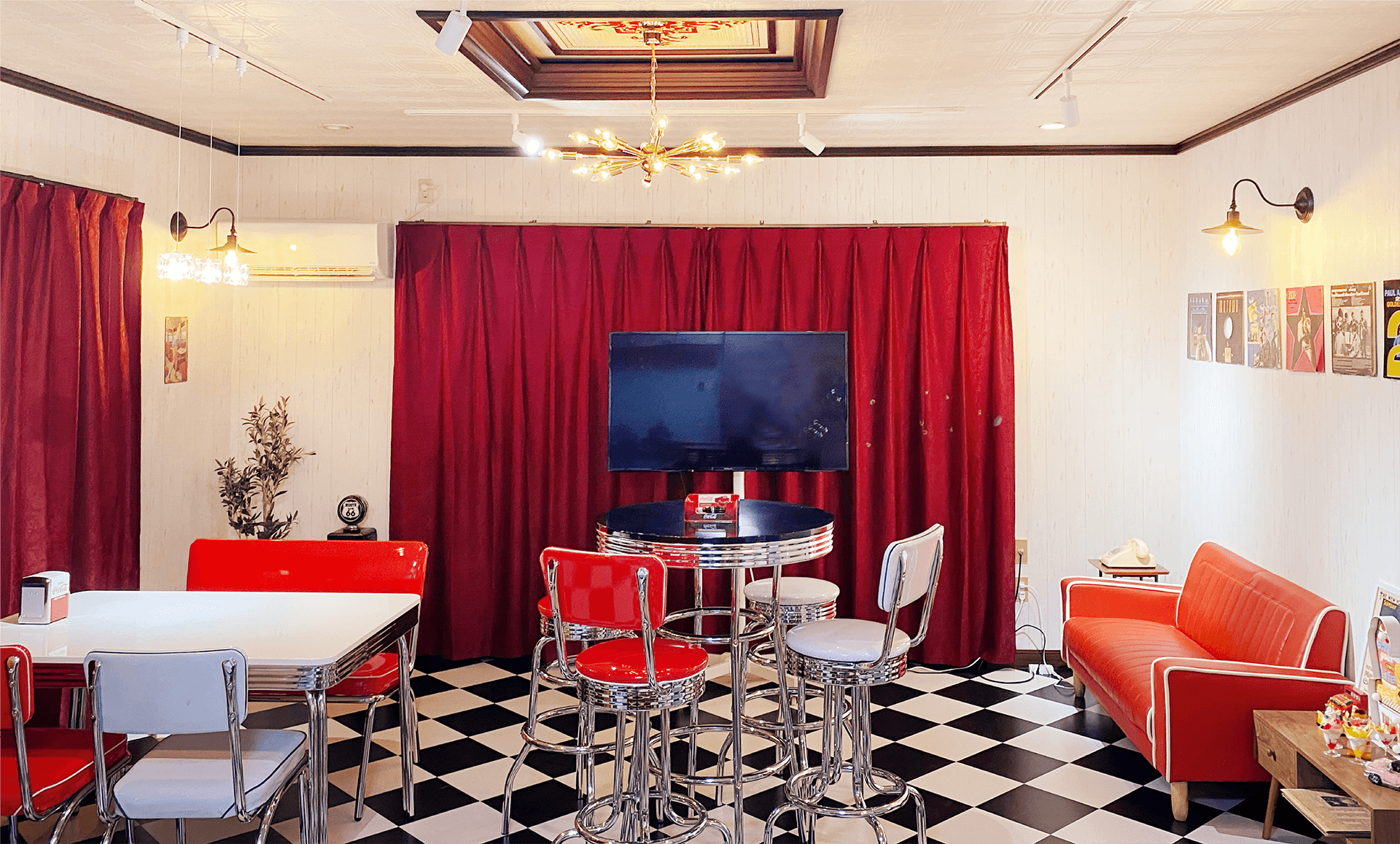 チェック柄の床に無地の赤いカーテン。アメリカンダイナーなチェアやスツール、テーブルがある部屋全体の内観